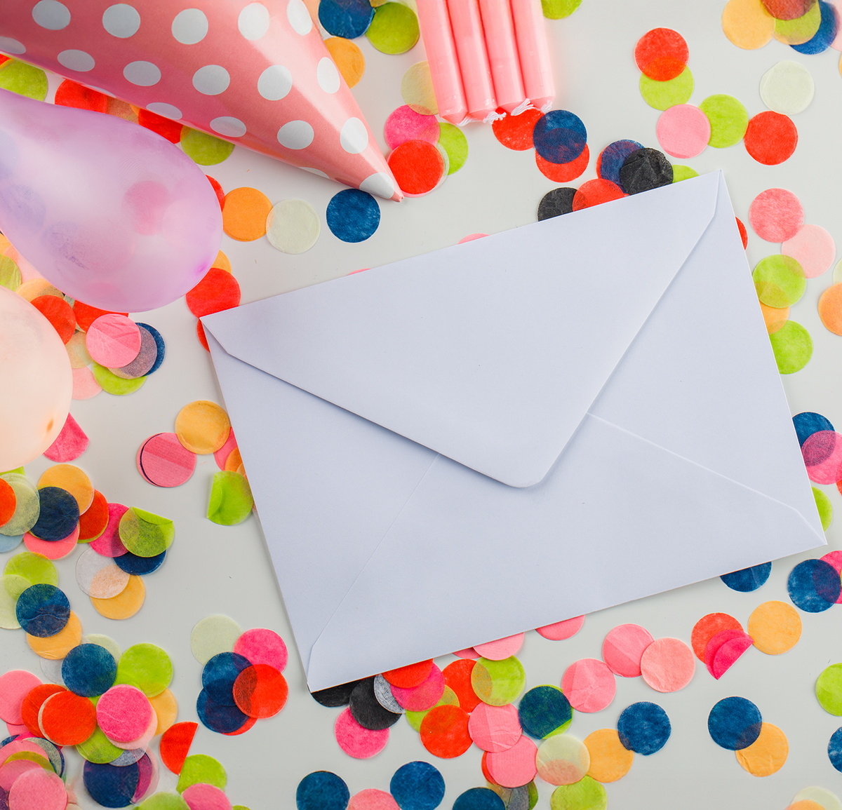 White envelope on a colorful confetti background with balloons