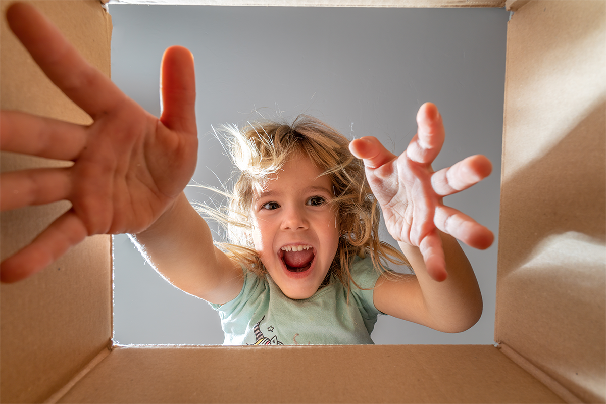 Child reaching out from a cardboard box with excitement