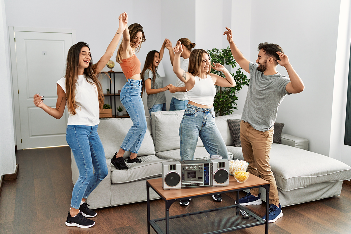 Group of friends dancing in a living room with a boombox.