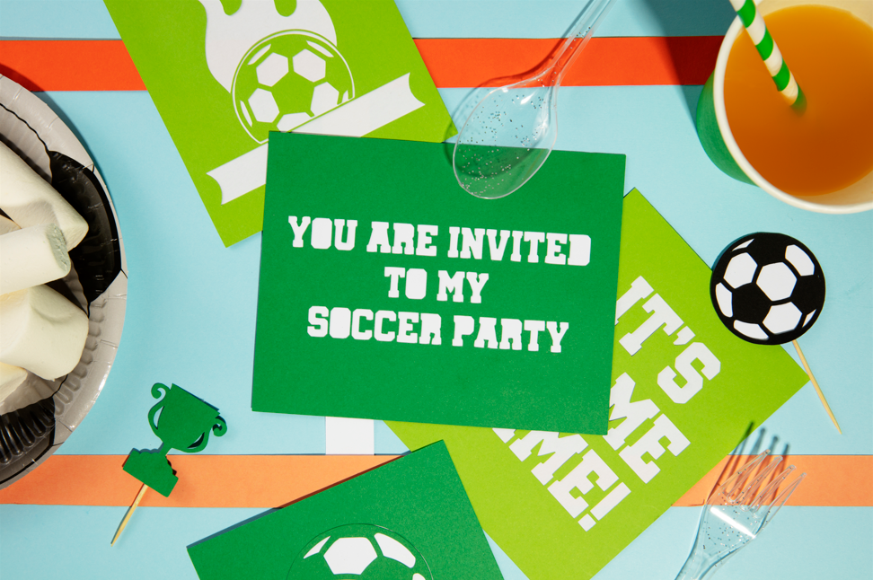 Green invitation card for a soccer party on a colorful table with party decorations.