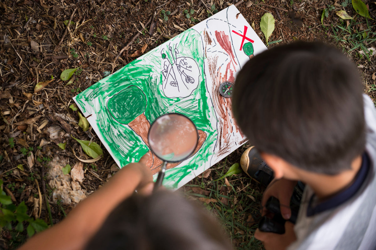 Child using a magnifying glass to examine a nature-themed drawing outdoors.