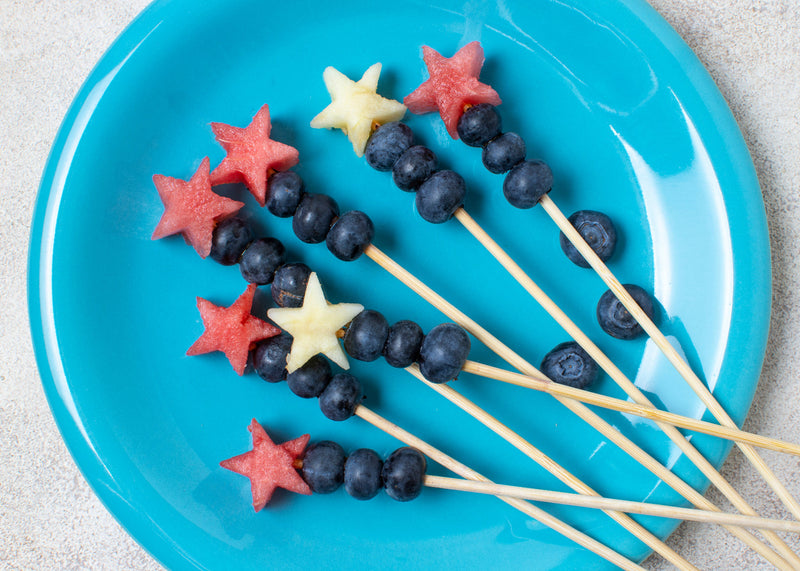 Fruit skewers shaped like a firework on a blue plate.