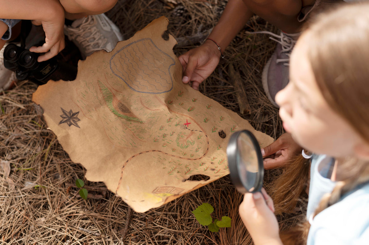 Children examining a treasure map with a magnifying glass on the ground.
