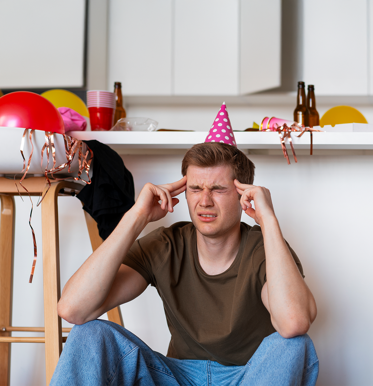 Man wearing a party hat with a distressed expression in a kitchen setting