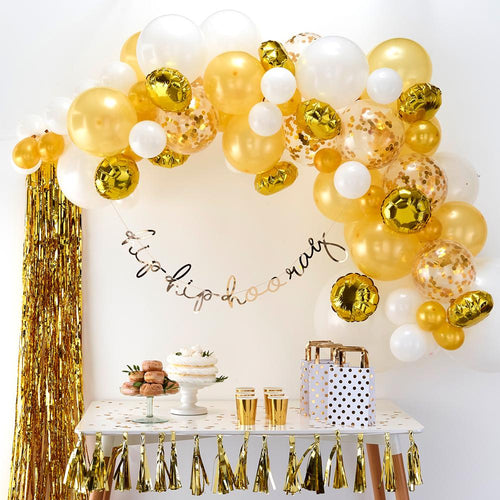 A party table with a large gold balloon arch hung up above it