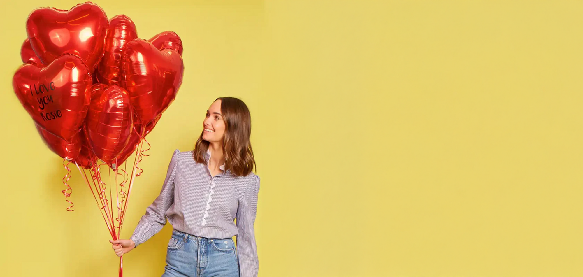 Woman holding red heart-shaped balloons against a yellow background