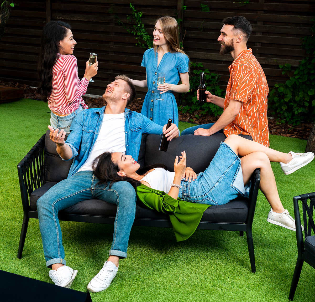 Group of friends socializing on a black outdoor sofa with drinks.