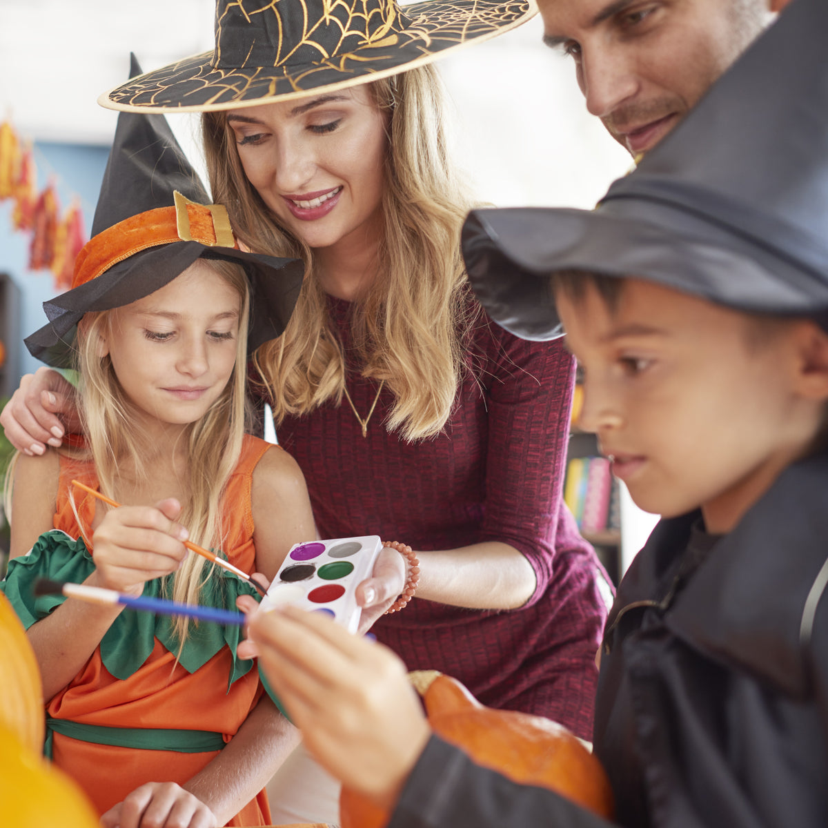 Family of four, two adults and two children, engaged in pumpkin carving with Halloween costumes.