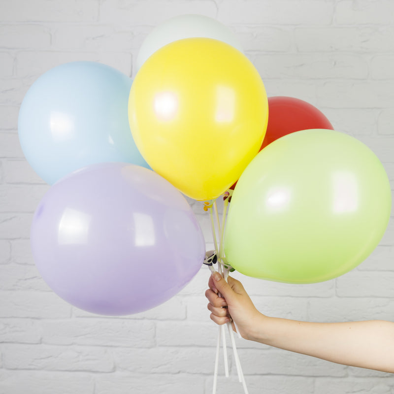 Hand holding a bunch of colorful balloons against a light gray brick wall.