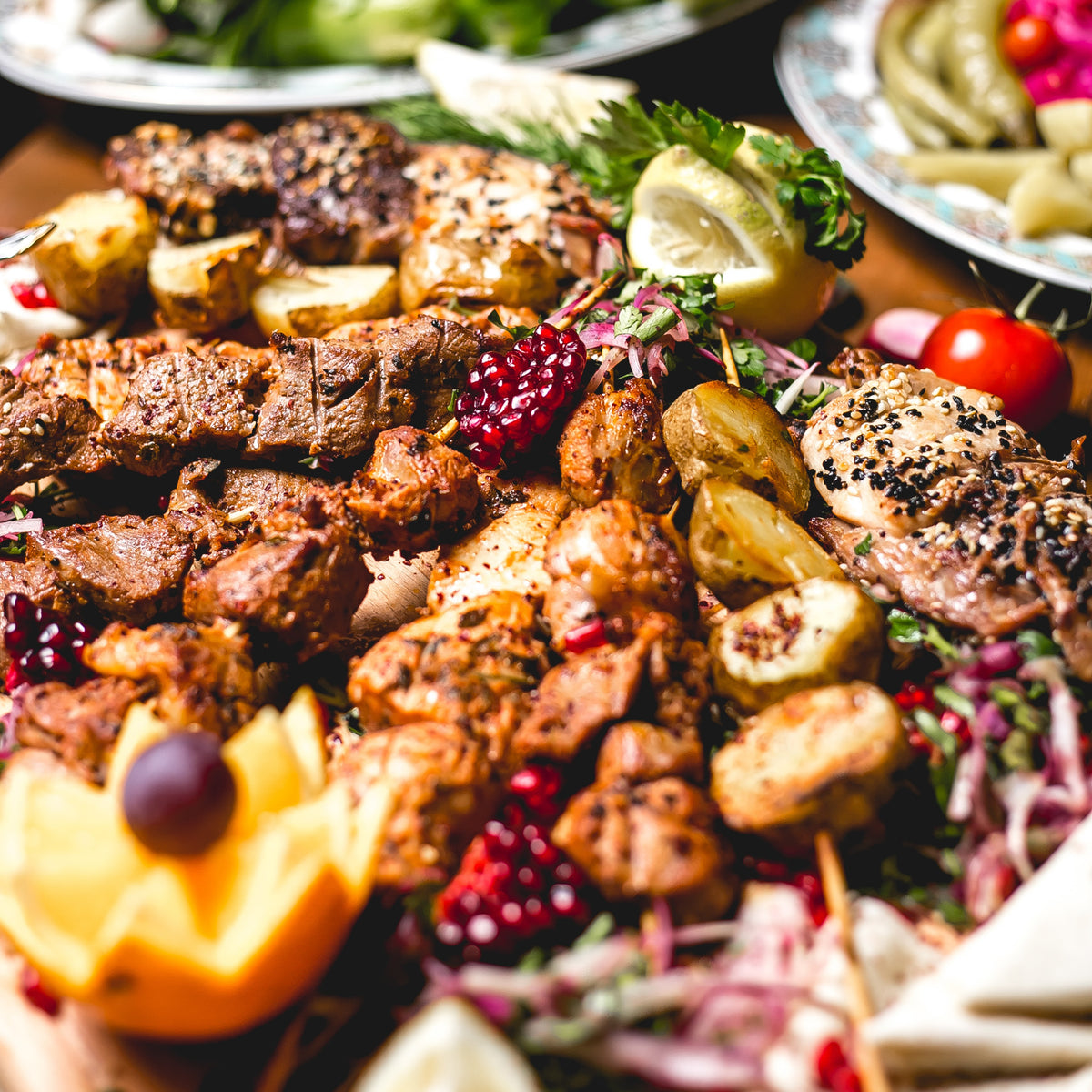 Plated dish with grilled meats, vegetables, and garnishes on a wooden table.