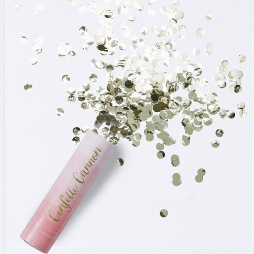 A pink pastel confetti cannon firing a burst of shiny gold foil confetti