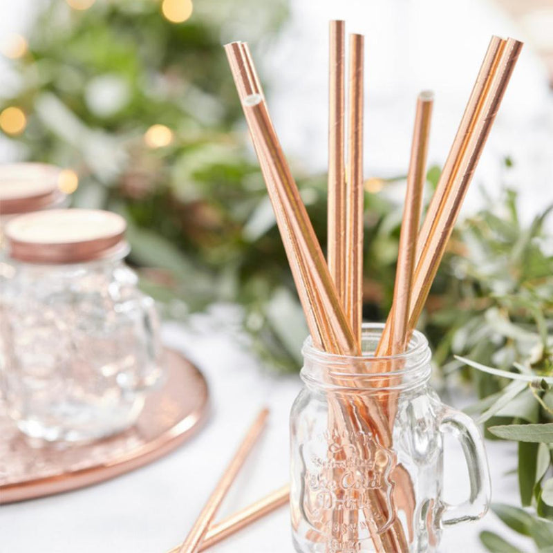 A glass jar filled with shiny, rose gold-foiled paper party straws