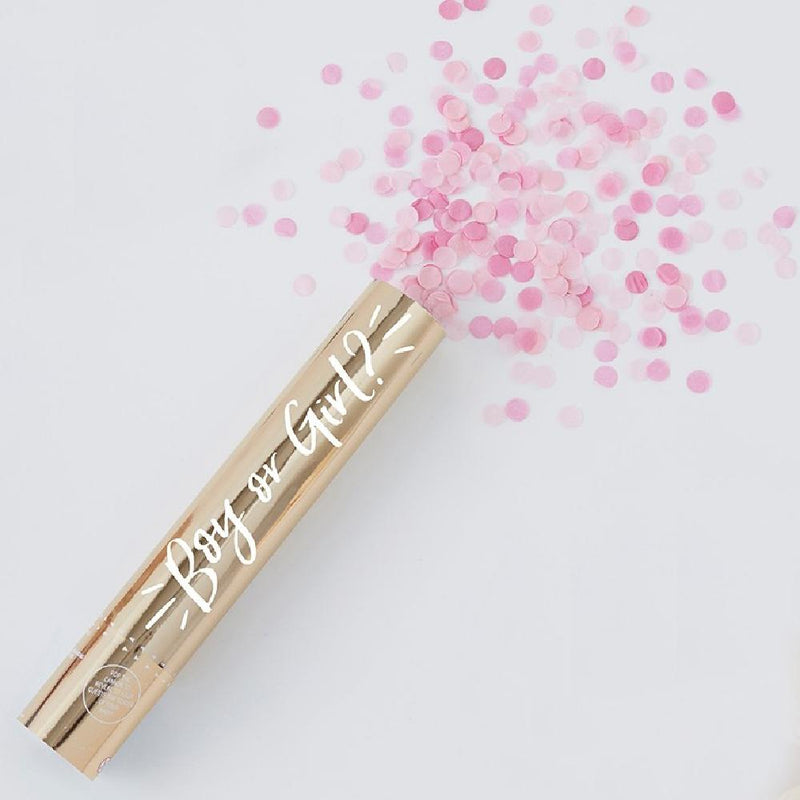 A gold gender reveal confetti cannon with a burst of pink confetti shooting out the top