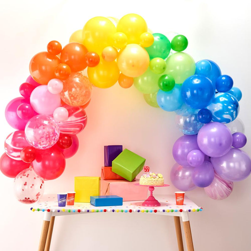 A balloon arch with rainbow colours placed above a party table