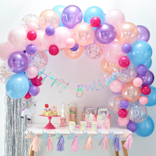 A large balloon arch with pastel-coloured balloons placed above a party table